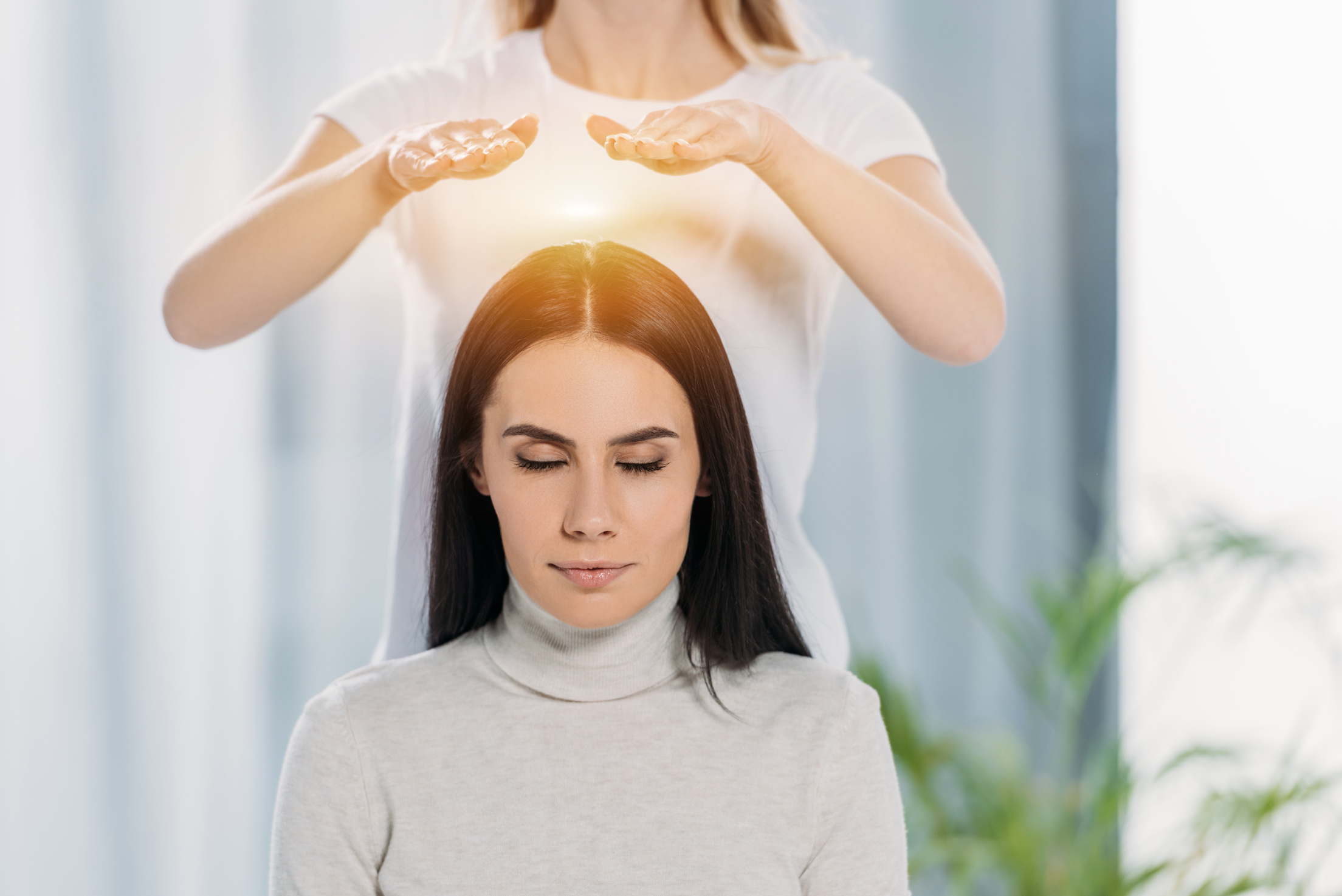 peaceful young woman with closed eyes receiving reiki healing therapy above head