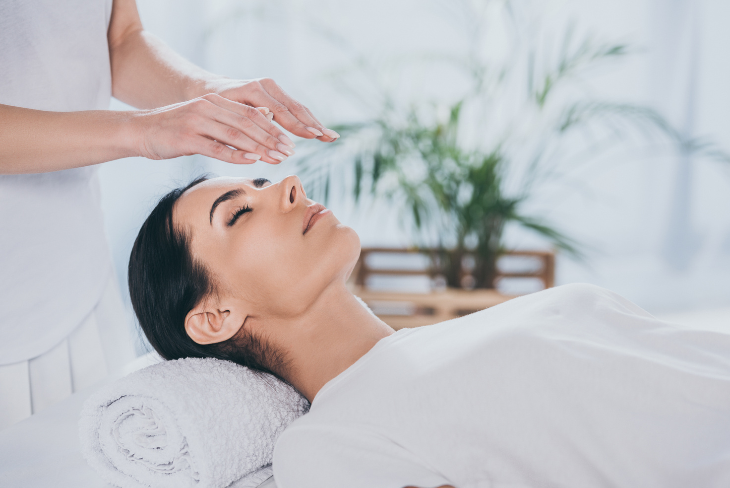 cropped shot of calm young woman with closed eyes receiving reiki treatment above head